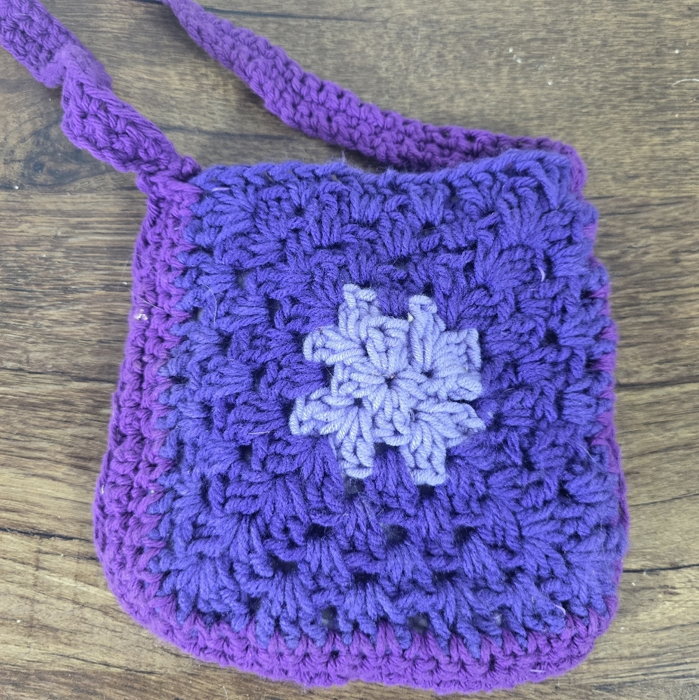 small crocheted purple granny square crossbody bag with a light purple flower